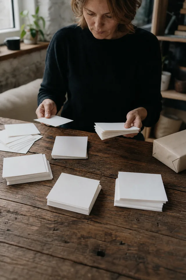 Maker sorting blank envelopes or cards beside a neutral parcel.