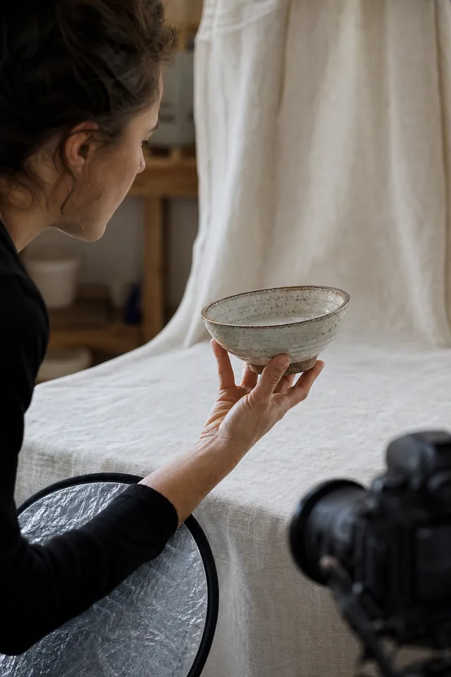 A photographer examines a single bowl against a cloth backdrop.