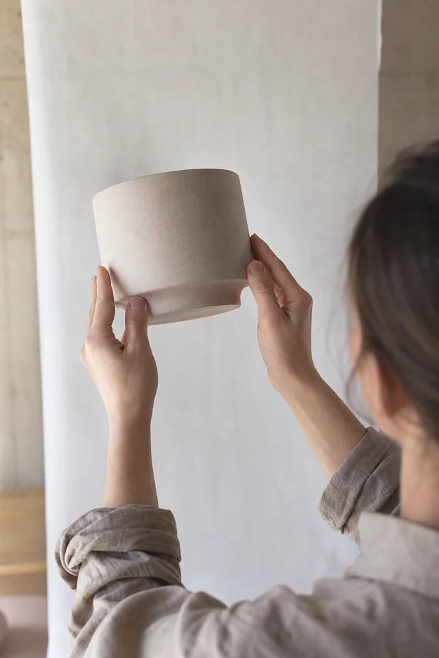 Hands hold a simple ceramic product against a plain background.