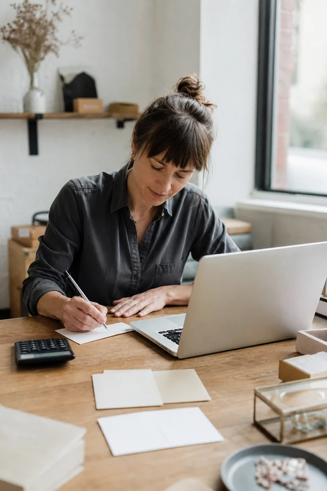 AI-generated editorial photograph of a maker writing a decision note beside a laptop and calculator.